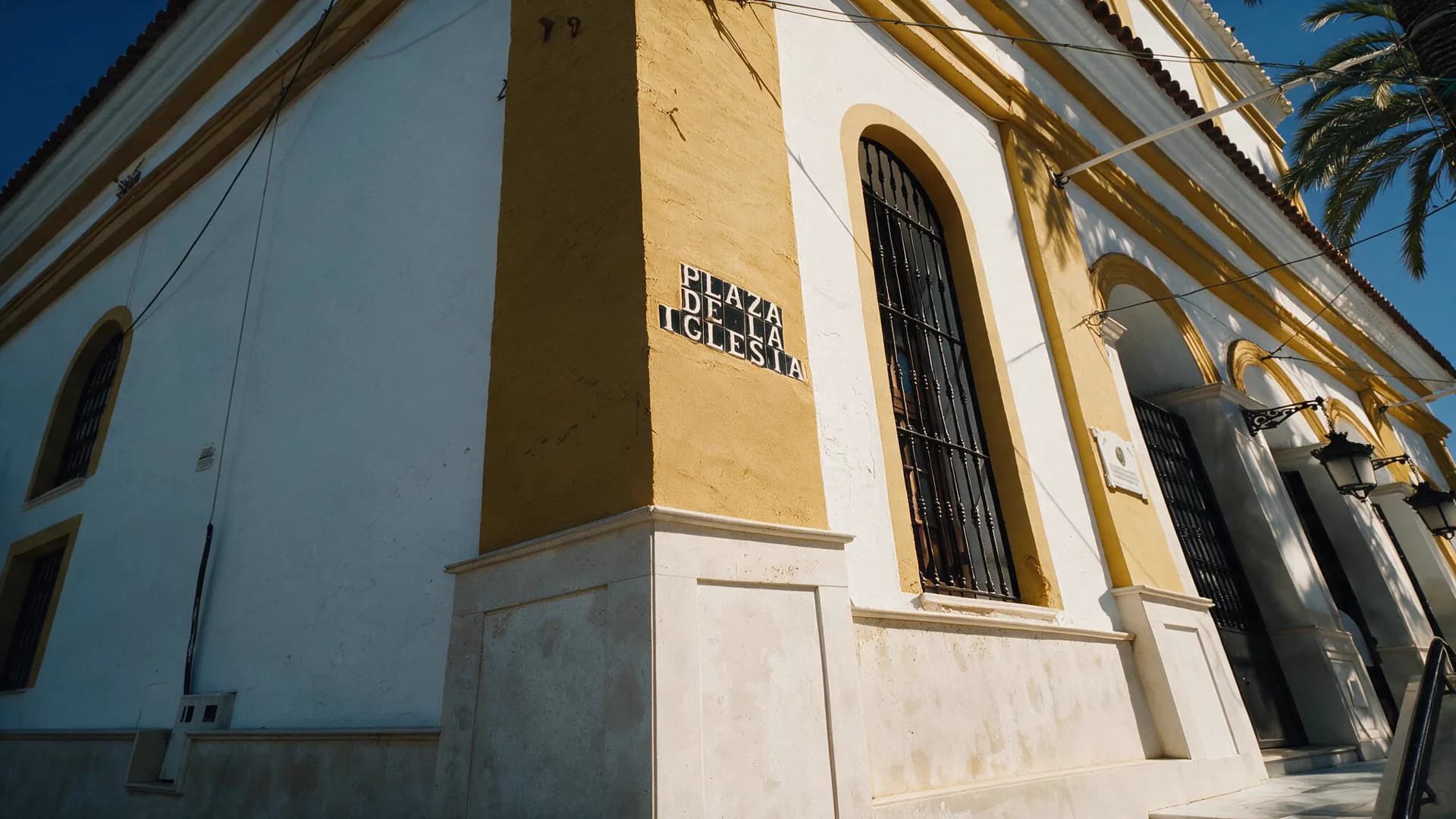Fachada blanca y amarilla de la iglesia con el rótulo de la Plaza de la Iglesia